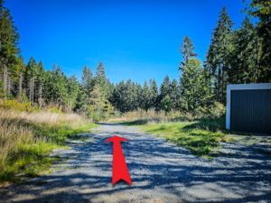 An einer Garage mit Wegweisern vorbei in den Wald